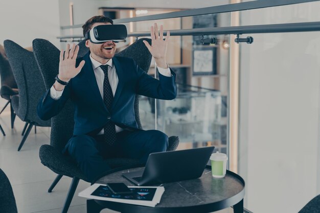 Uomo d'affari vestito con un abito formale che indossa occhiali vr mentre lavora al computer portatile al bar