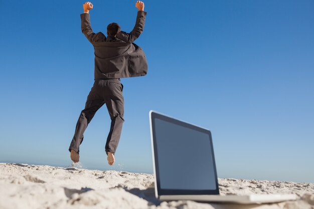 Uomo d&#39;affari vittorioso che salta lasciando il suo computer portatile