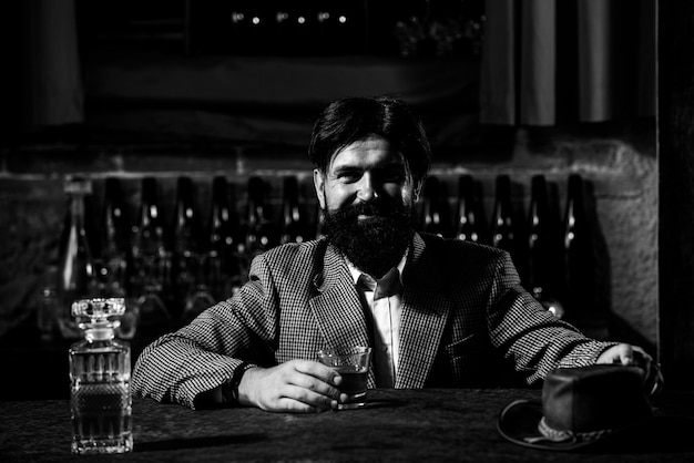 Uomo d'epoca lavoratore con barba lunga che tiene whisky seduto al bar