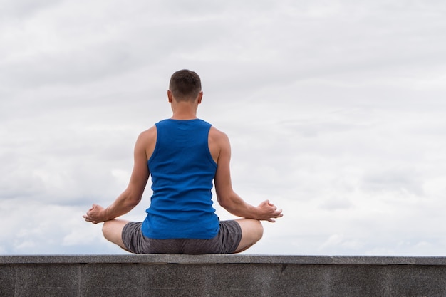 Uomo da dietro seduto nella posa yoga del loto e meditando