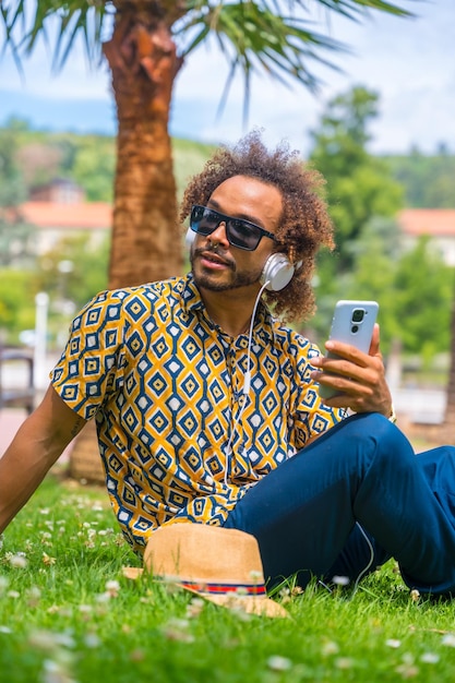 Uomo dai capelli afro in vacanza estiva accanto ad alcune palme sulla spiaggia Concetto di viaggio e turismo ascoltando mucisca con le cuffie