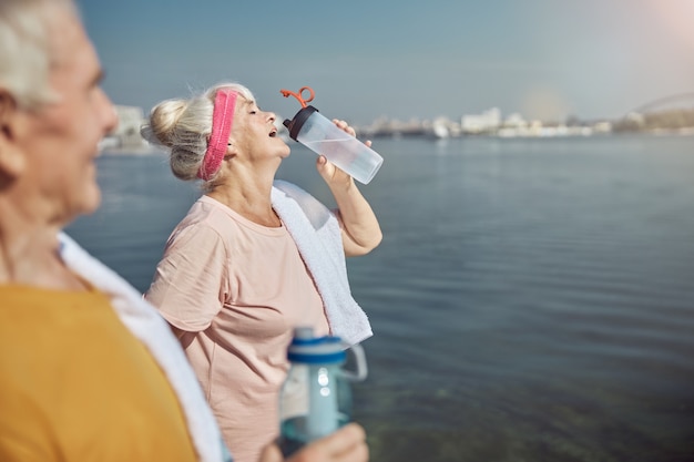 Uomo dai capelli grigi che guarda una signora anziana che beve acqua da una bottiglia di plastica in mano