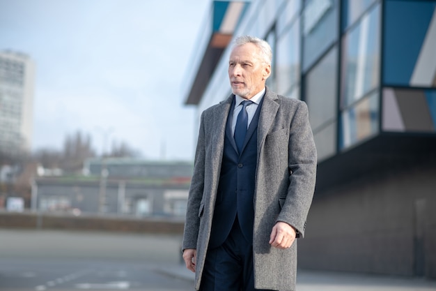 Uomo dai capelli grigi che indossa un cappotto grigio in piedi vicino all'ufficio