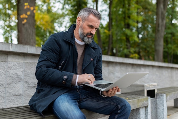 Uomo dai capelli grigi che lavora su un computer portatile nel parco