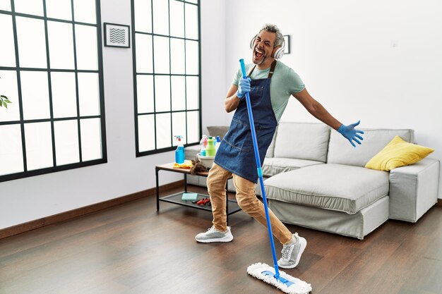 Uomo dai capelli grigi di mezza età che canta una canzone usando il mop come microfono a casa