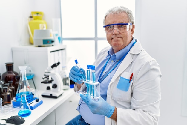 Uomo dai capelli grigi di mezza età che indossa un'uniforme da scienziato che tiene la provetta in laboratorio