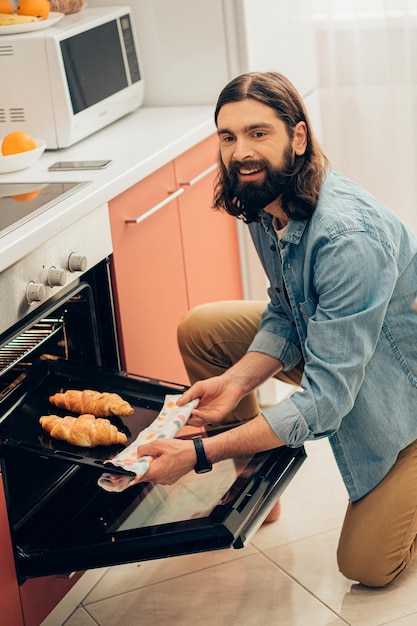 Uomo dai capelli lunghi barbuto allegro che sorride e prende due croissant caldi dal forno
