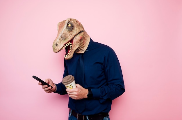 Uomo dalla testa di dinosauro con una tazza di caffè e uno smartphone.