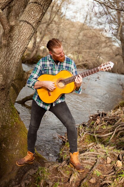 Uomo dei pantaloni a vita bassa con la barba rossa con una chitarra nel campo