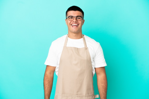 Uomo del cameriere del ristorante sopra fondo blu isolato con l'espressione facciale di sorpresa