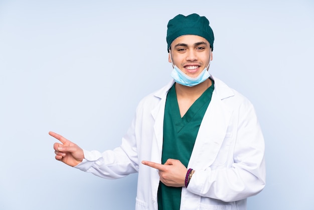 Uomo del chirurgo con uniforme isolato su sfondo blu che punta il dito a lato