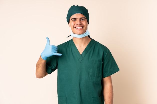 Uomo del chirurgo in uniforme blu sopra fondo isolato che fa gesto del telefono