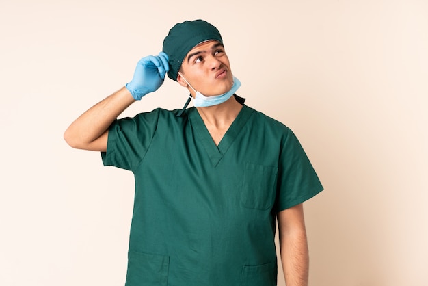 Uomo del chirurgo in uniforme blu sopra la parete che ha dubbi e con espressione faccia confusa