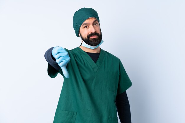 Uomo del chirurgo in uniforme verde sopra la parete che mostra pollice giù con l'espressione negativa