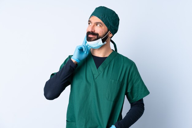 Uomo del chirurgo in uniforme verde sopra la parete che pensa un'idea mentre guardando su