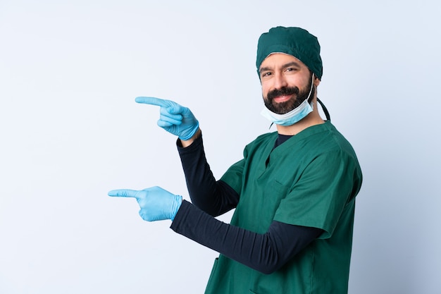 Uomo del chirurgo in uniforme verde sopra la parete isolata che indica barretta al lato e che presenta un prodotto