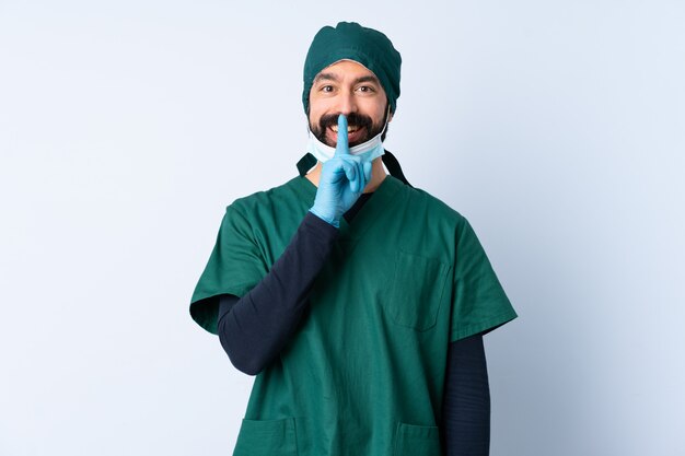 Uomo del chirurgo in uniforme verde sopra la parete isolata che mostra un segno di gesto di silenzio che mette il dito in bocca