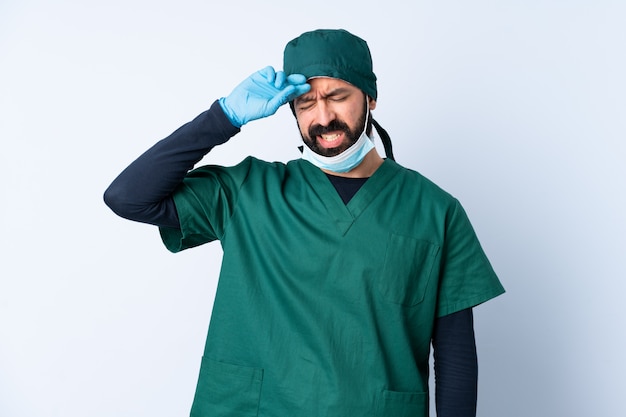 Uomo del chirurgo in uniforme verde sopra la parete isolata con l'espressione stanca e malata