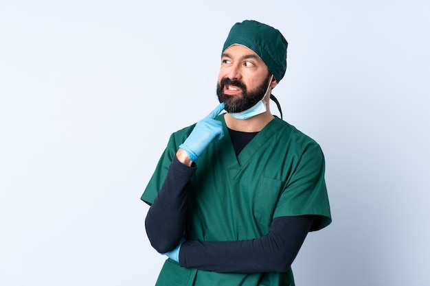 Uomo del chirurgo in uniforme verde sopra la parete isolata nervosa e spaventata
