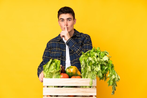 Uomo del coltivatore dell'adolescente con le verdure di recente selezionate in una scatola che fa gesto di silenzio