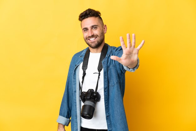 Uomo del fotografo isolato sulla parete gialla che conta cinque con le dita