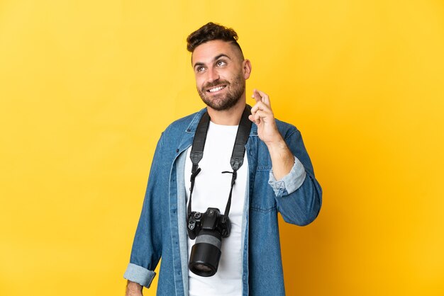 Uomo del fotografo isolato sulla parete gialla con le dita che incrociano e che desiderano il meglio