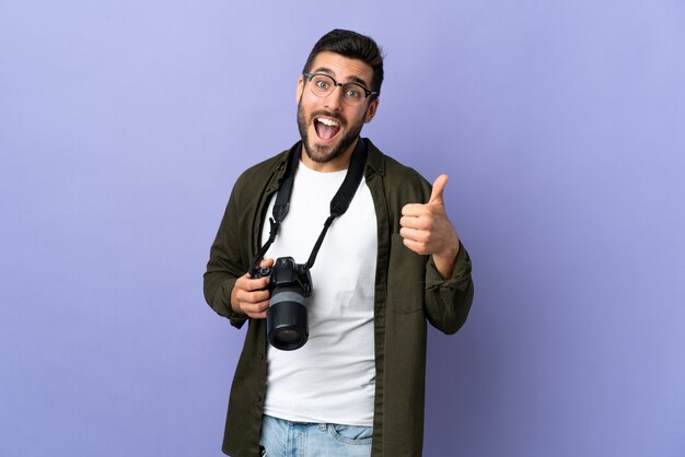 Uomo del fotografo sopra la parete viola isolata con i pollici in su perché è successo qualcosa di buono