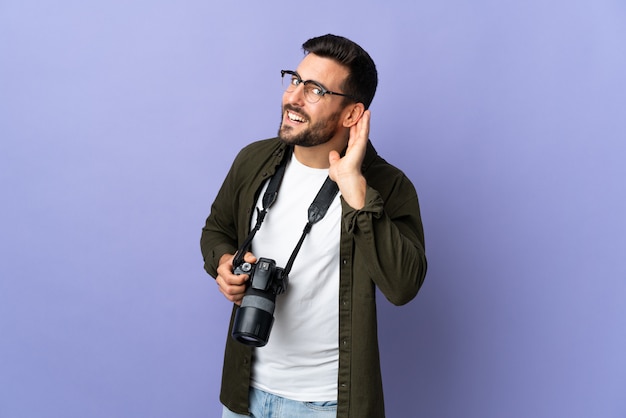 Uomo del fotografo sopra la porpora isolata che ascolta qualcosa mettendo la mano sull'orecchio