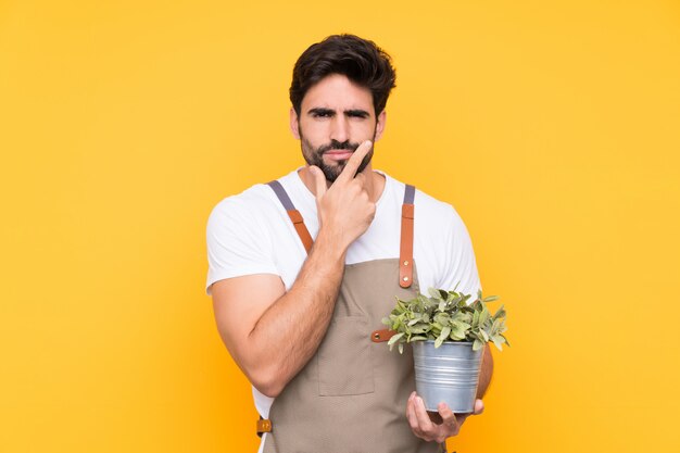 Uomo del giardiniere con la barba sopra la parete gialla isolata che pensa un'idea