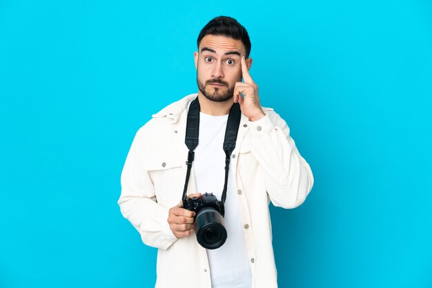 Uomo del giovane fotografo isolato sulla parete blu che pensa un'idea