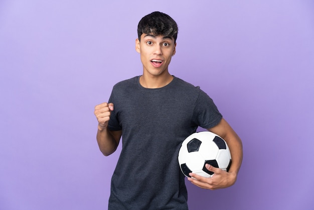 Uomo del giovane giocatore di football americano sopra la parete viola isolata che celebra una vittoria nella posizione del vincitore