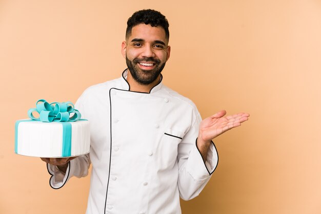 Uomo del giovane panettiere latino che tiene una torta che mostra qualcosa