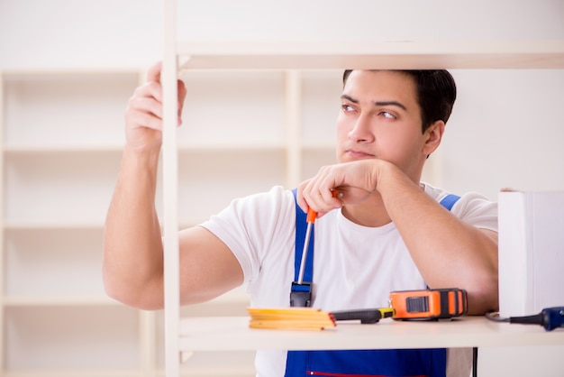 Uomo del lavoratore che ripara lo scaffale per libri di montaggio