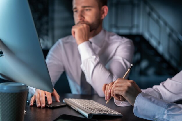 Uomo del manager dell'ufficio che pensa davanti al monitor del computer primo piano delle mani con la tastiera Manager maschio sfocato in camicia bianca con la partner femminile con la matita Concetto di lavoro di squadra