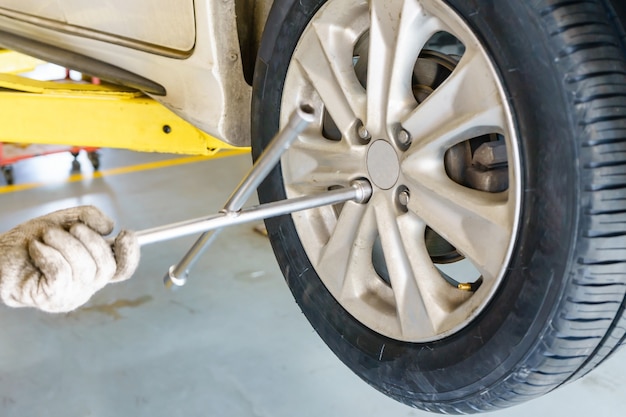 Uomo del meccanico con il cacciavite elettrico che cambia gomma all&#39;officina