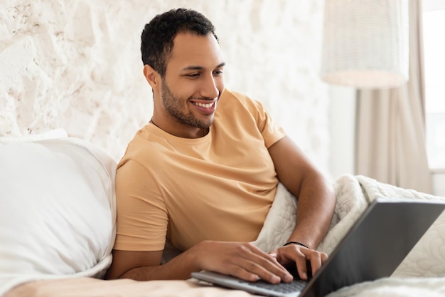 Uomo del Medio Oriente che utilizza il laptop sdraiato a letto in camera da letto