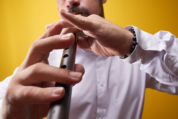 Uomo del musicista professionista che gioca un primo piano del tubo in uno studio giallo. Strumento a fiato popolare, flauto