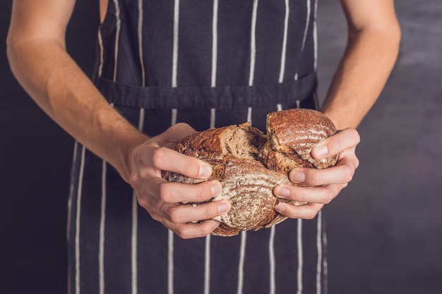 Uomo del panettiere che tiene in mano pane di grano rustico fatto in casa. Messa a fuoco selettiva