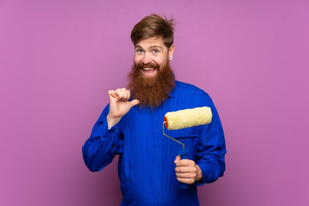 Uomo del pittore con la barba lunga sopra la parete viola isolata fiera e soddisfatta di sé