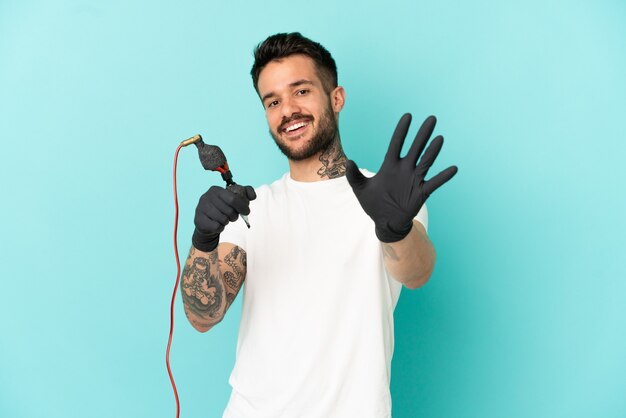 Uomo del tatuatore sopra fondo blu isolato che saluta con la mano con l'espressione felice