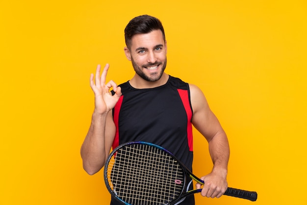 Uomo del tennis sopra la parete gialla isolata che mostra segno giusto con le dita