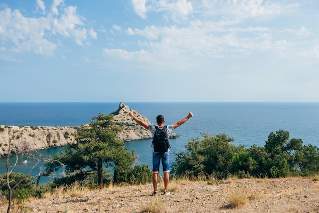 Uomo del viaggiatore con lo zaino che sta con le mani sollevate sulla natura