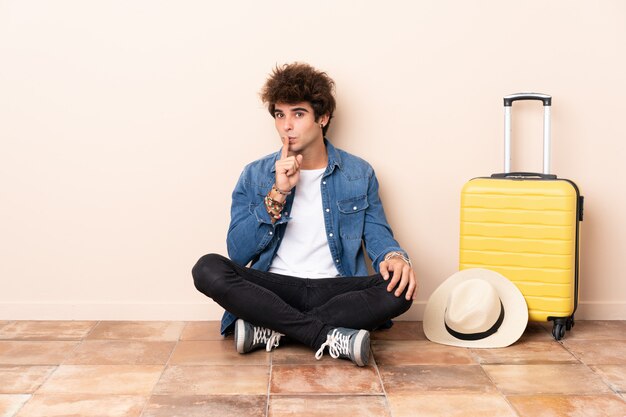 Uomo del viaggiatore la sua valigia che si siede sul pavimento che fa gesto di silenzio