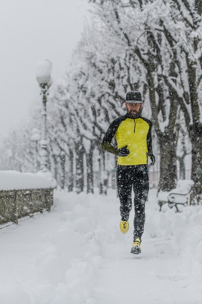 Uomo dell'atleta corre su un marciapiede della città durante forti nevicate