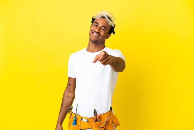 Uomo dell'elettricista afroamericano sopra la parete gialla isolata che indica la parte anteriore con l'espressione felice