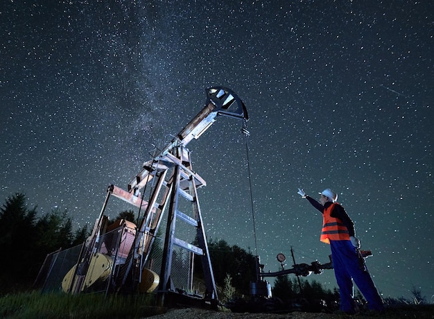 Uomo dell'olio in piedi vicino al martinetto della pompa sotto il cielo stellato notturno