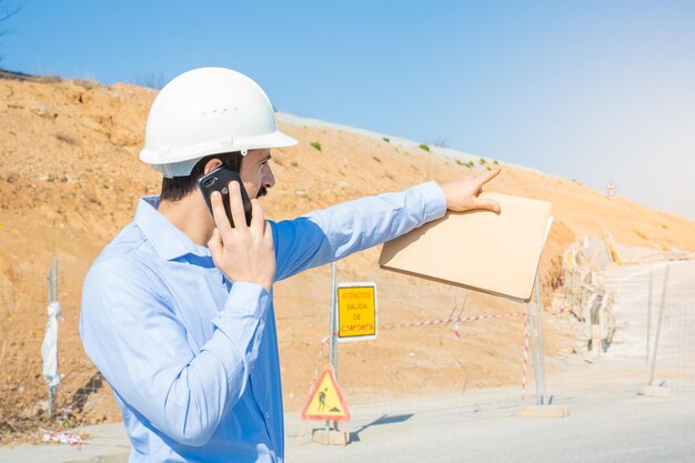 Uomo della costruzione con casco bianco che lavora con il telefono