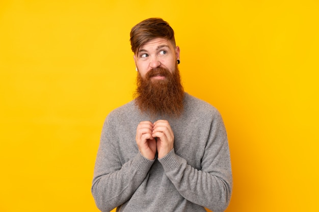 Uomo della testarossa con la barba lunga sopra la parete gialla isolata che traccia qualcosa