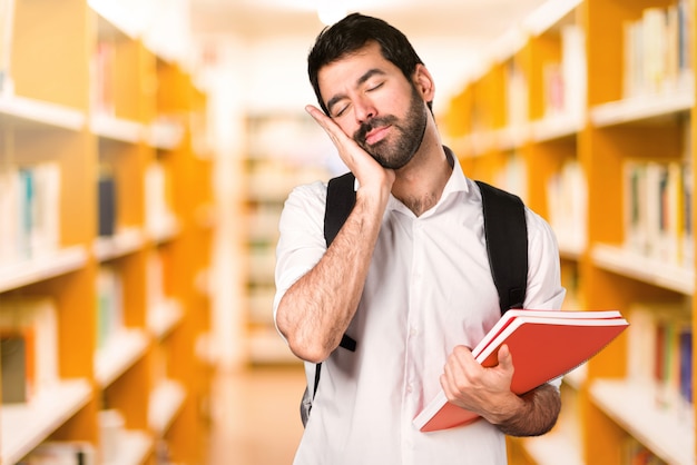 Uomo dello studente che fa gesto di sonno sulla biblioteca defocused