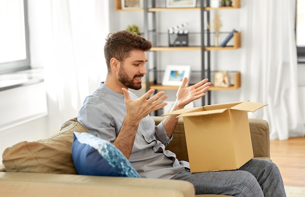 uomo deluso che apre una scatola di pacchi a casa